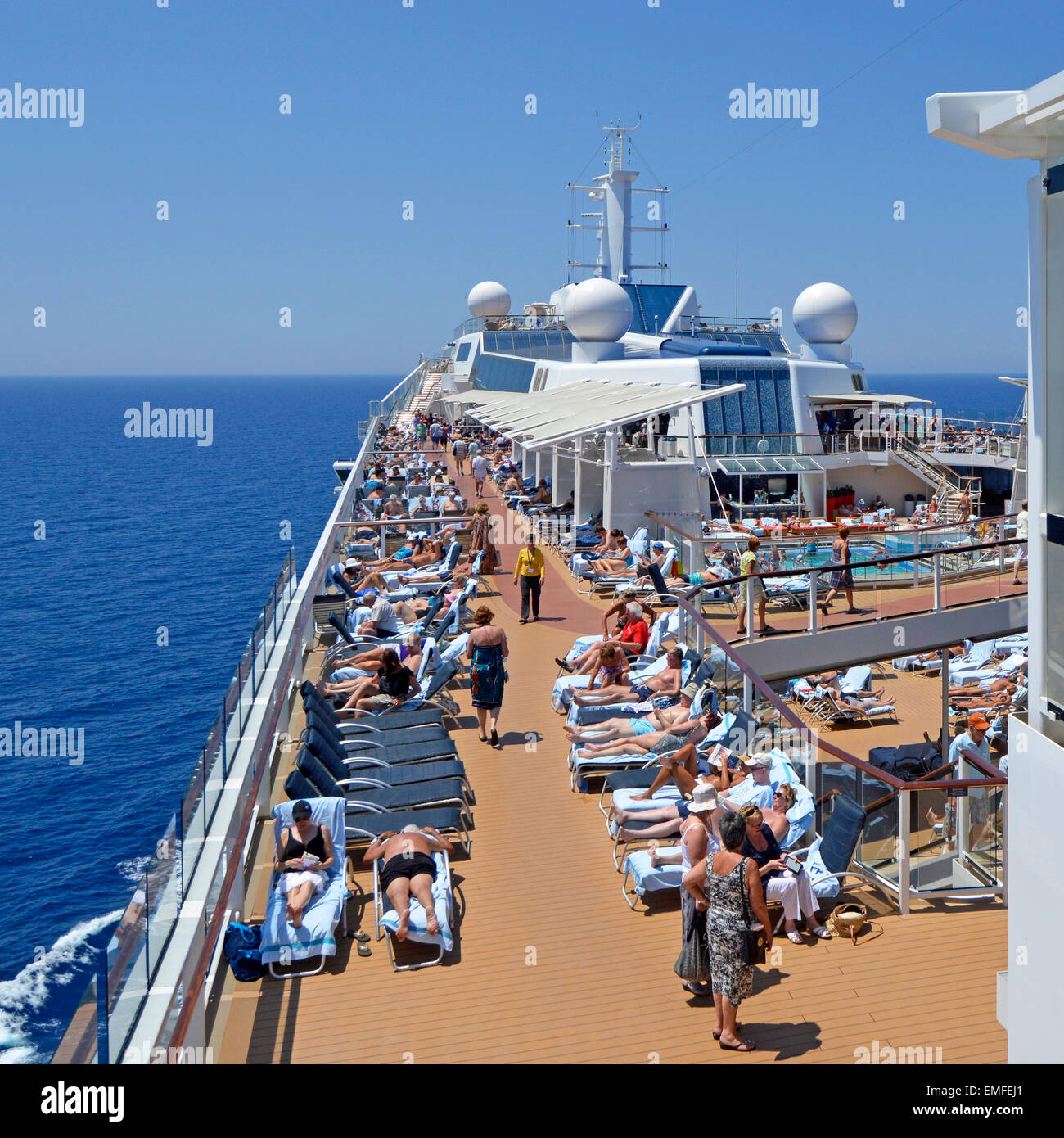 Vue vers le bas sur les bains de soleil occupés et le pont de la piscine sur le paquebot de croisière océanique pendant une journée ensoleillée de ciel bleu en mer naviguant sur la Méditerranée Banque D'Images