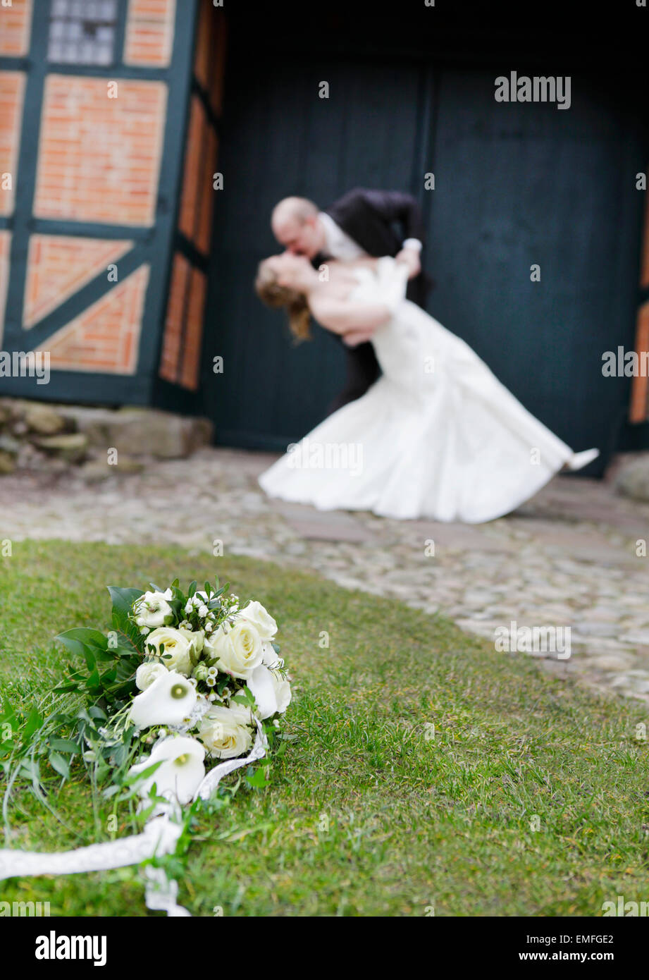 Un bouquet de roses blanches dans l'herbe. Dans l'arrière-plan un kissing Bride and Groom Banque D'Images