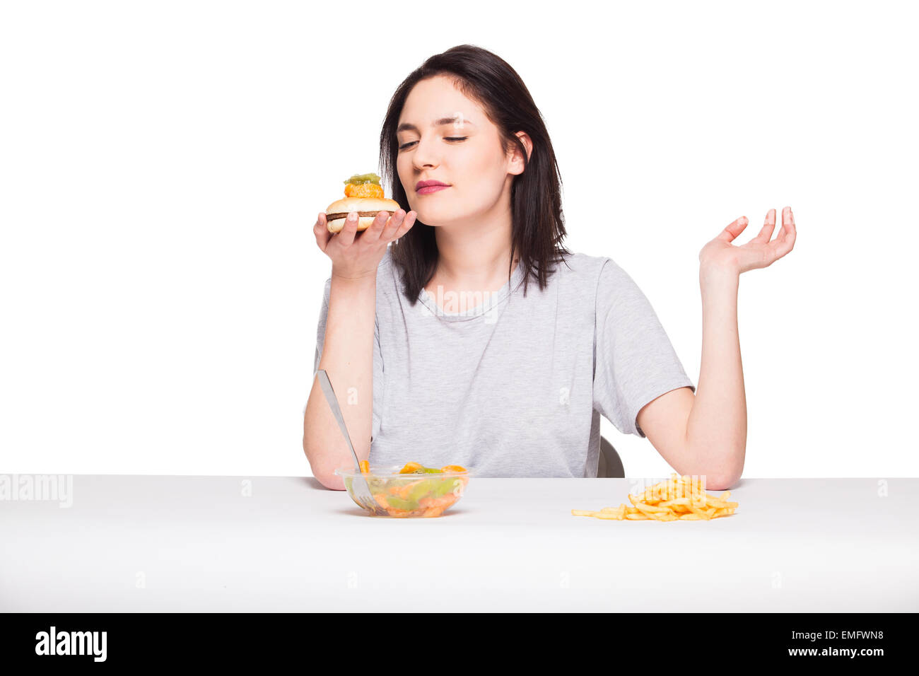 Par rapport à la malbouffe santé concept avec une femme naturelle en attrape les fruits avant les repas et le choix de frites avec hamburger, isolé o Banque D'Images