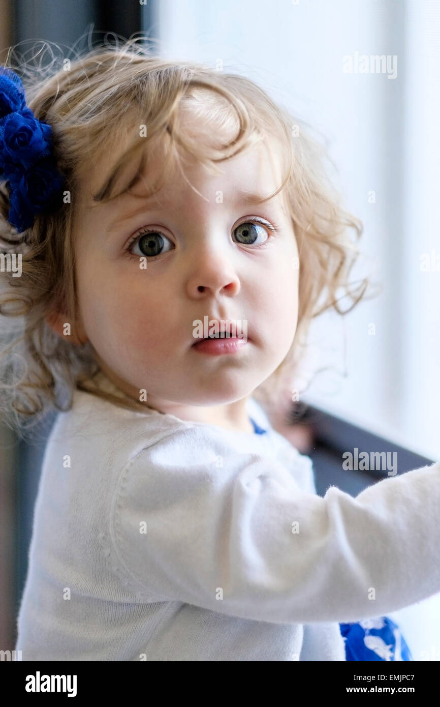 Une belle fille de race blanche de 14 mois se tient près d'une porte avec une belle lumière du nord looking at camera. USA Banque D'Images