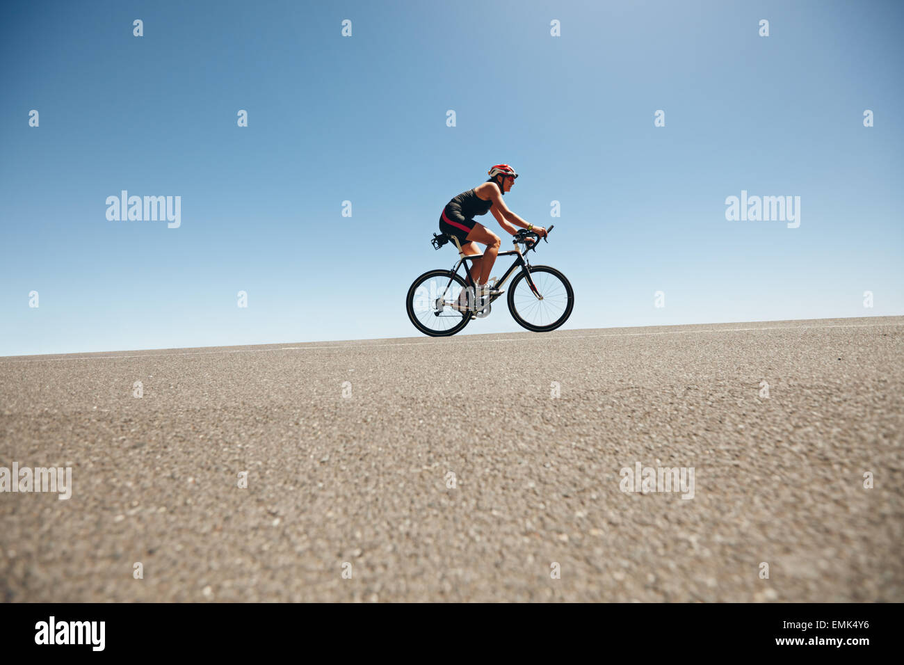 Cycliste féminine sur une route de campagne la formation pour le triathlon. Young woman riding bicycle jusqu'à la colline. Banque D'Images