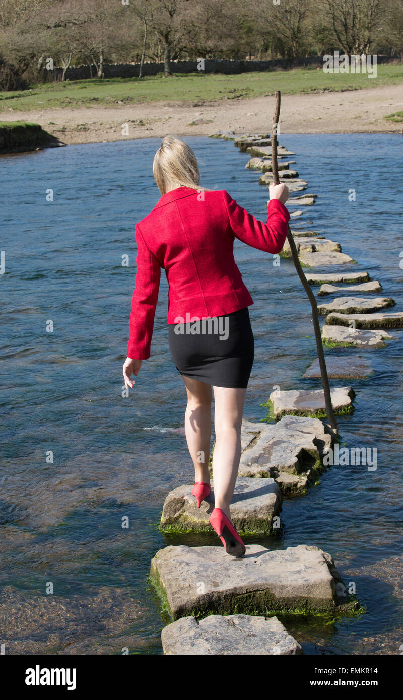 Stepping Stones smartly dressed woman crossing river à l'aide d'une branche d'arbre pour l'équilibre. Balade sur la rivière dans le sud de Ogmore W Banque D'Images