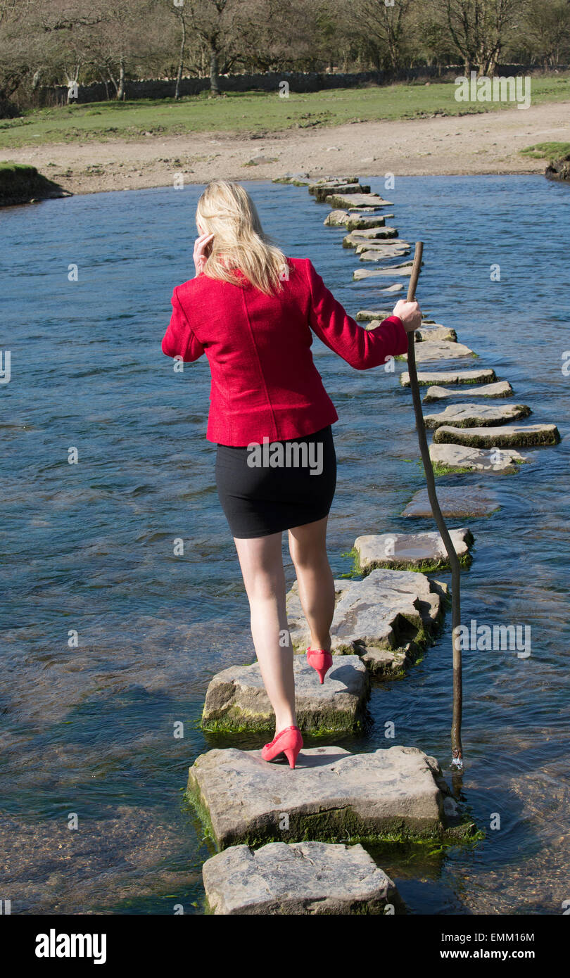 Stepping Stones smartly dressed woman crossing river à l'aide d'une branche d'arbre pour l'équilibre. Balade sur la rivière dans le sud de Ogmore W Banque D'Images