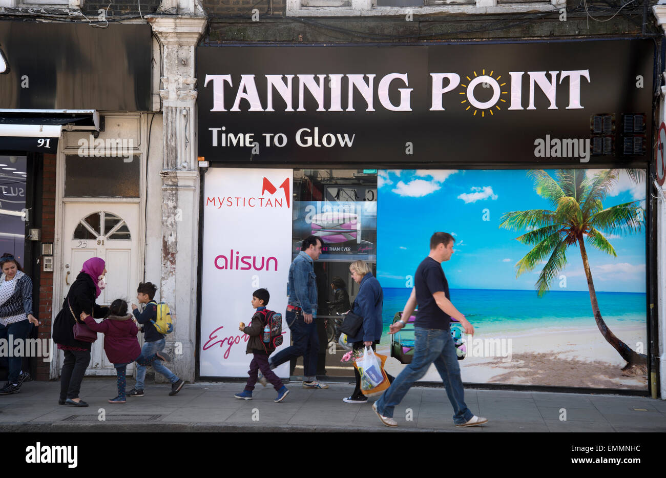 Hackney, Londres. Stoke Newington High Street. Solarium avec palm arbre photo et personnes marchant passé sur le trottoir Banque D'Images