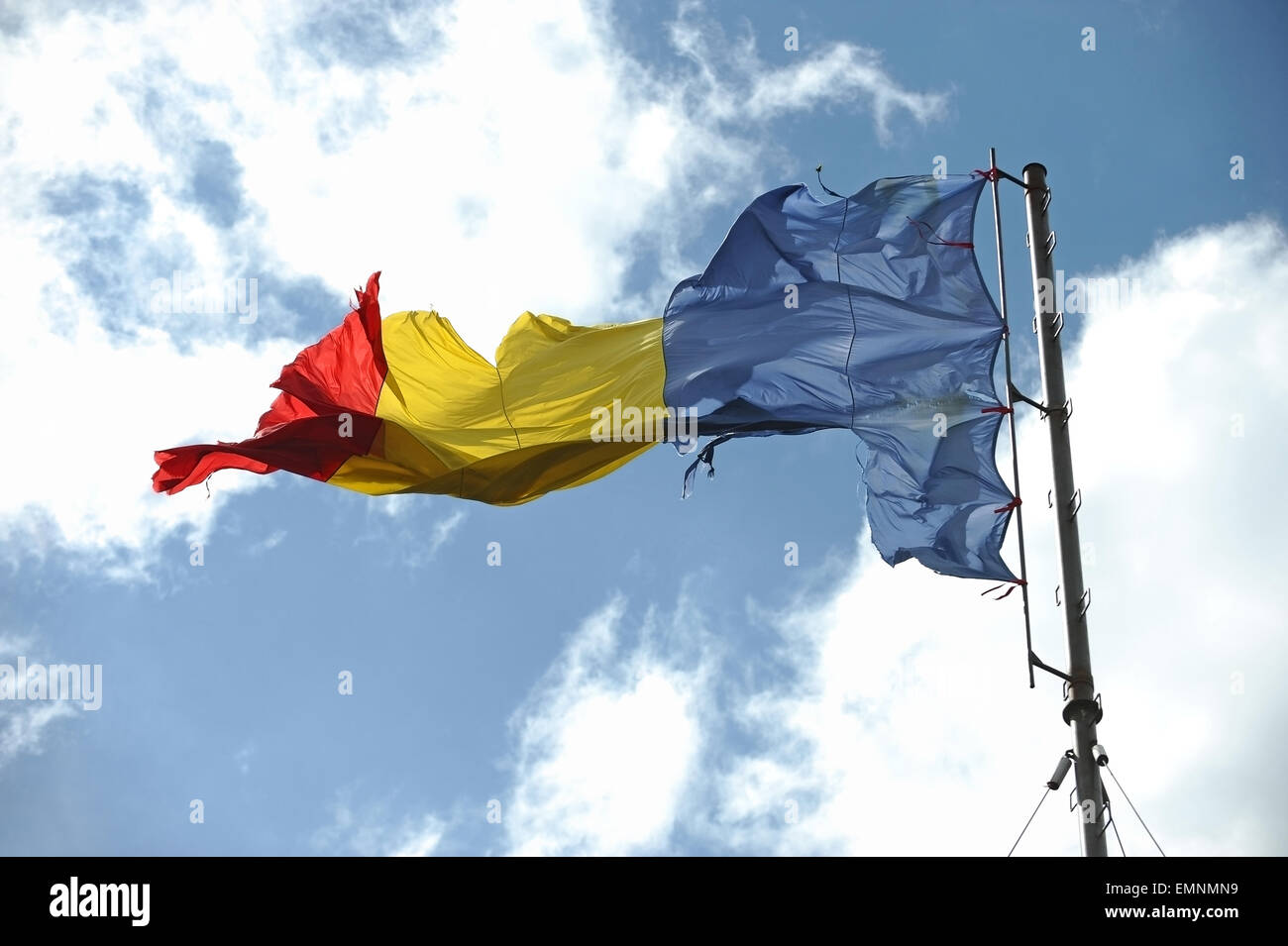 Drapeau roumain de déchiré par le vent avec ciel bleu sur l'arrière-plan Banque D'Images