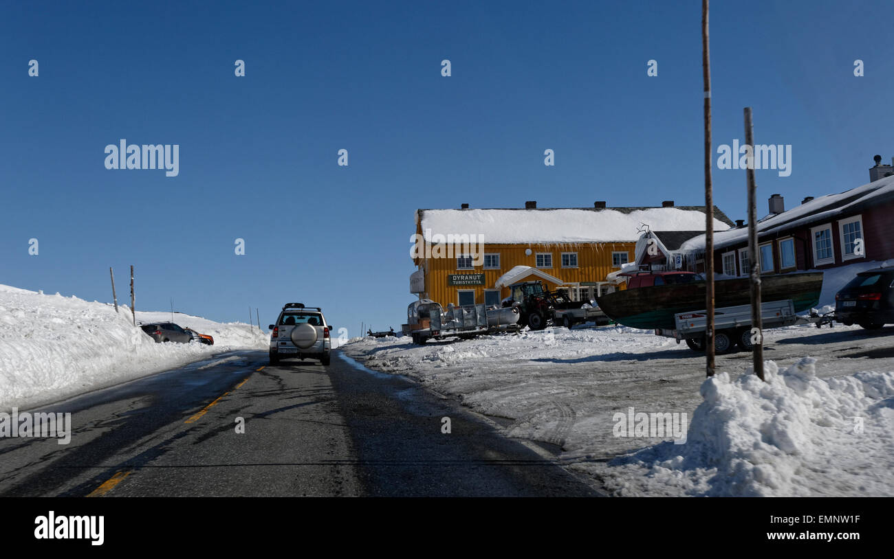 Voiture roulant en direction est sur la route E7 plus de Hardangervidda, passant Dyranut, Norvège, avec de hauts murs de neige entourant la route. Banque D'Images