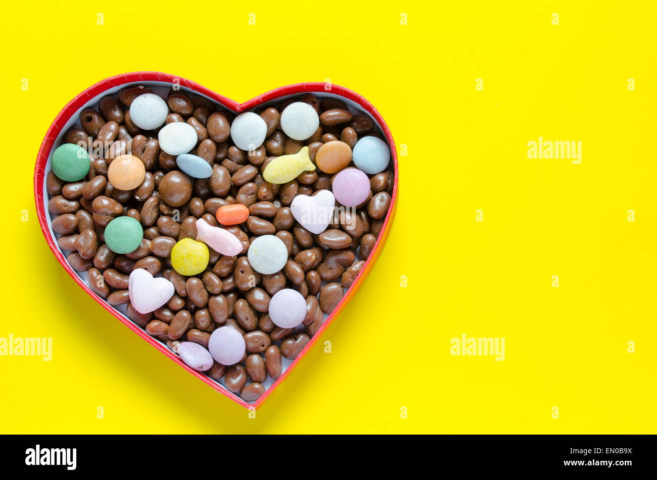 Boîte en forme de coeur rempli de petits chocolats boules avec beaucoup d'entre eux dispersés sur le fond jaune Banque D'Images