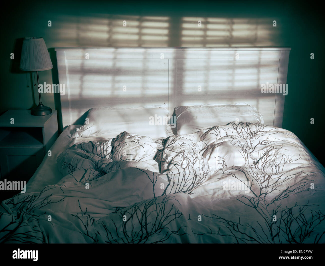 Unmade bed vide dramatique en faible lumière venant d'une fenêtre through blinds Banque D'Images
