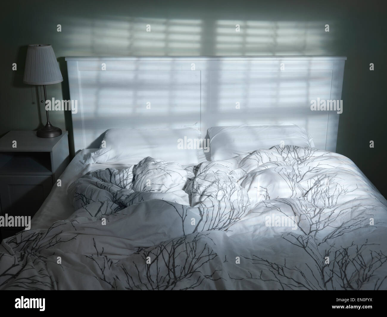Unmade bed vide dramatique en voyant à travers les stores Banque D'Images