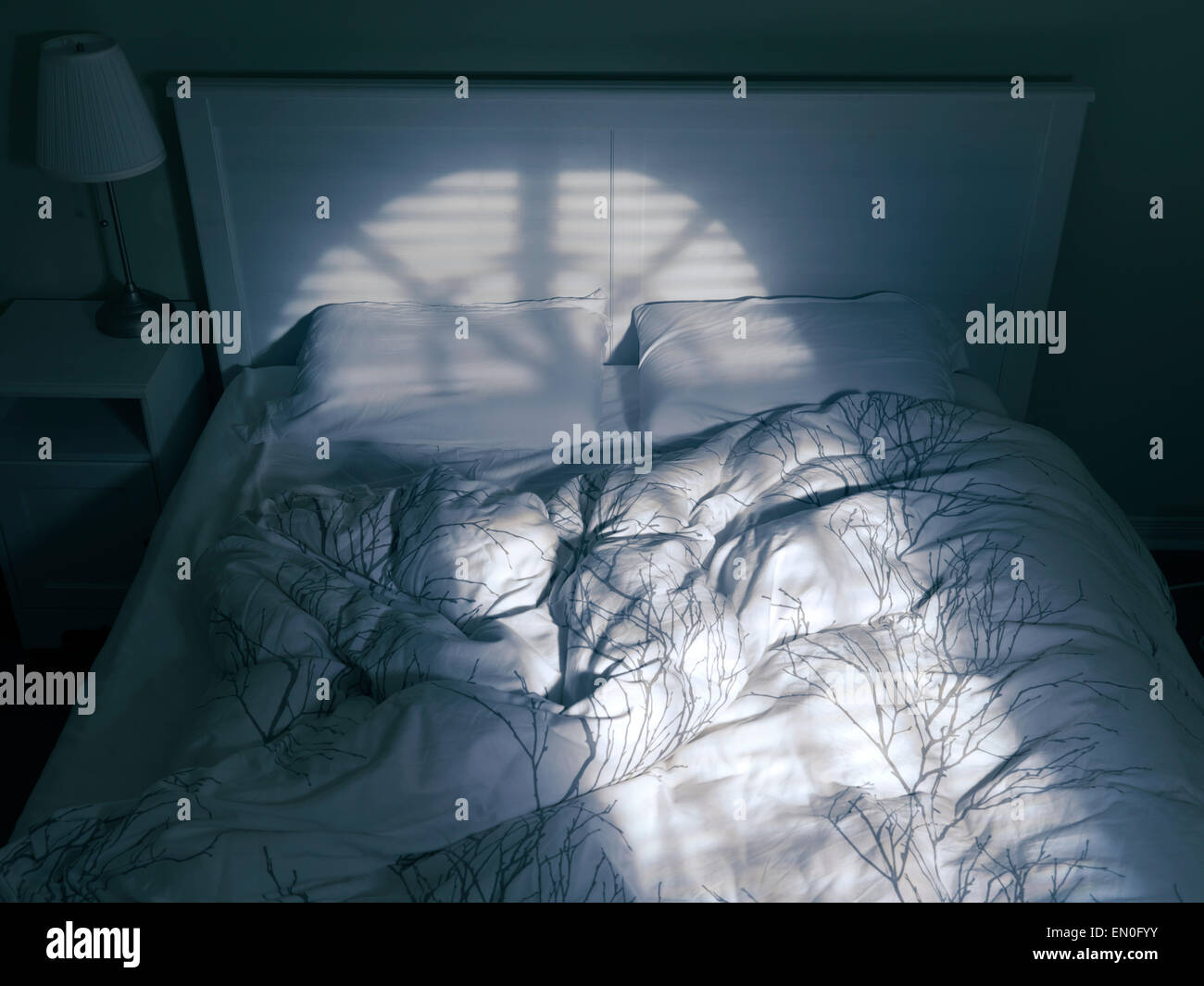 Unmade bed vide dans l'éclairage dramatique venant d'une fenêtre Banque D'Images