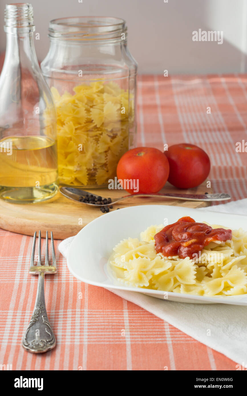 Farfalle à la sauce tomate sur le plat blanc, l'huile d'olive bouteille, bocal et verticale des tomates crues, selective focus Banque D'Images