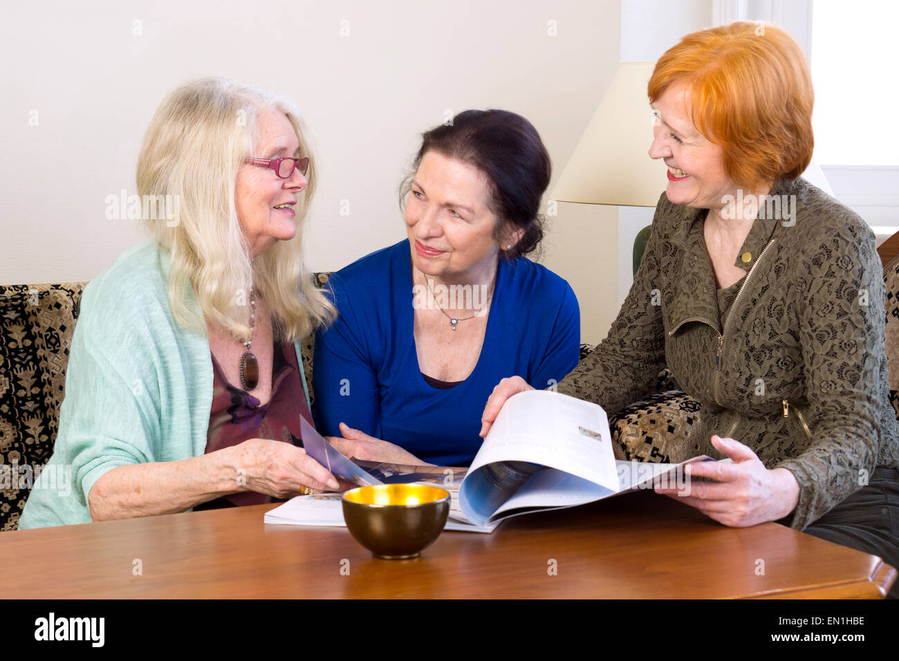 Trois femmes d'âge moyen Meilleurs amis jouissant de leurs pourparlers au Salon lors de la numérisation d'un magazine. Banque D'Images