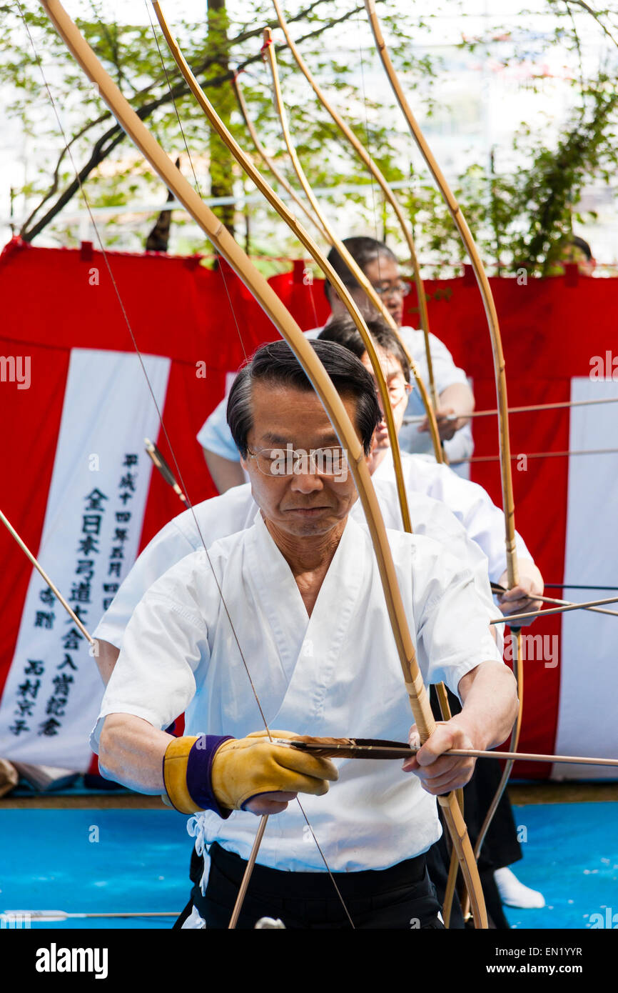 Des hommes japonais debout dans une rangée tirant des flèches d'arcs lors d'un concours de tir à l'arc pendant le festival annuel de Genji au sanctuaire de Tada, Osaka. Banque D'Images