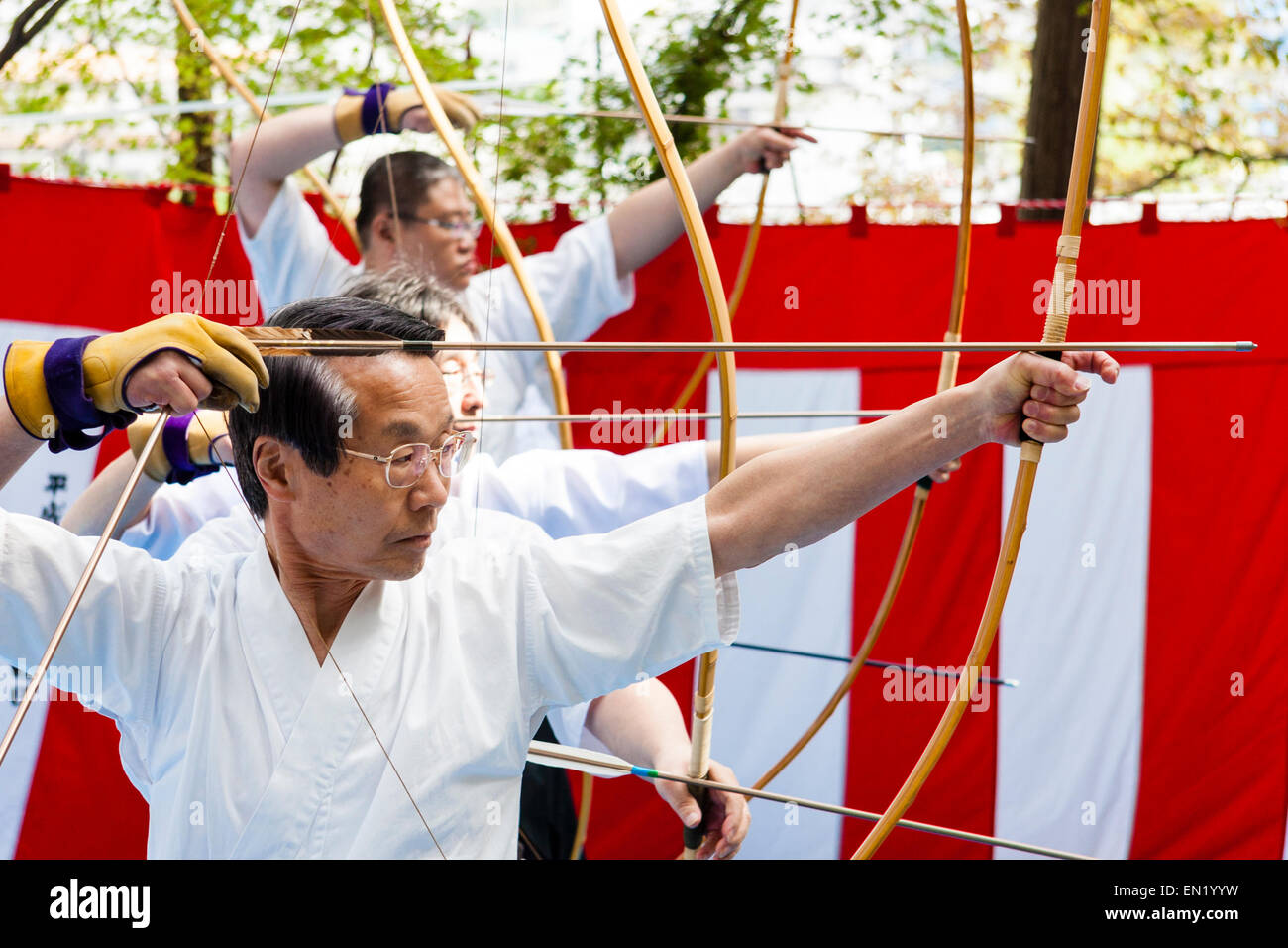 Des hommes japonais debout dans une rangée tirant des flèches d'arcs lors d'un concours de tir à l'arc pendant le festival annuel de Genji au sanctuaire de Tada, Osaka. Banque D'Images