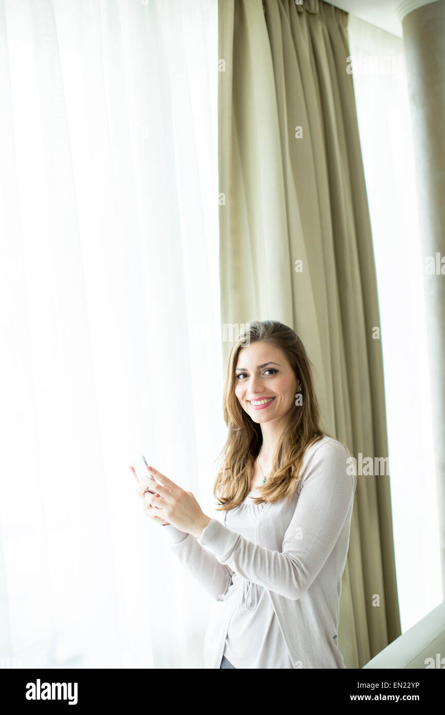 Jeune femme avec un téléphone mobile par la fenêtre Banque D'Images