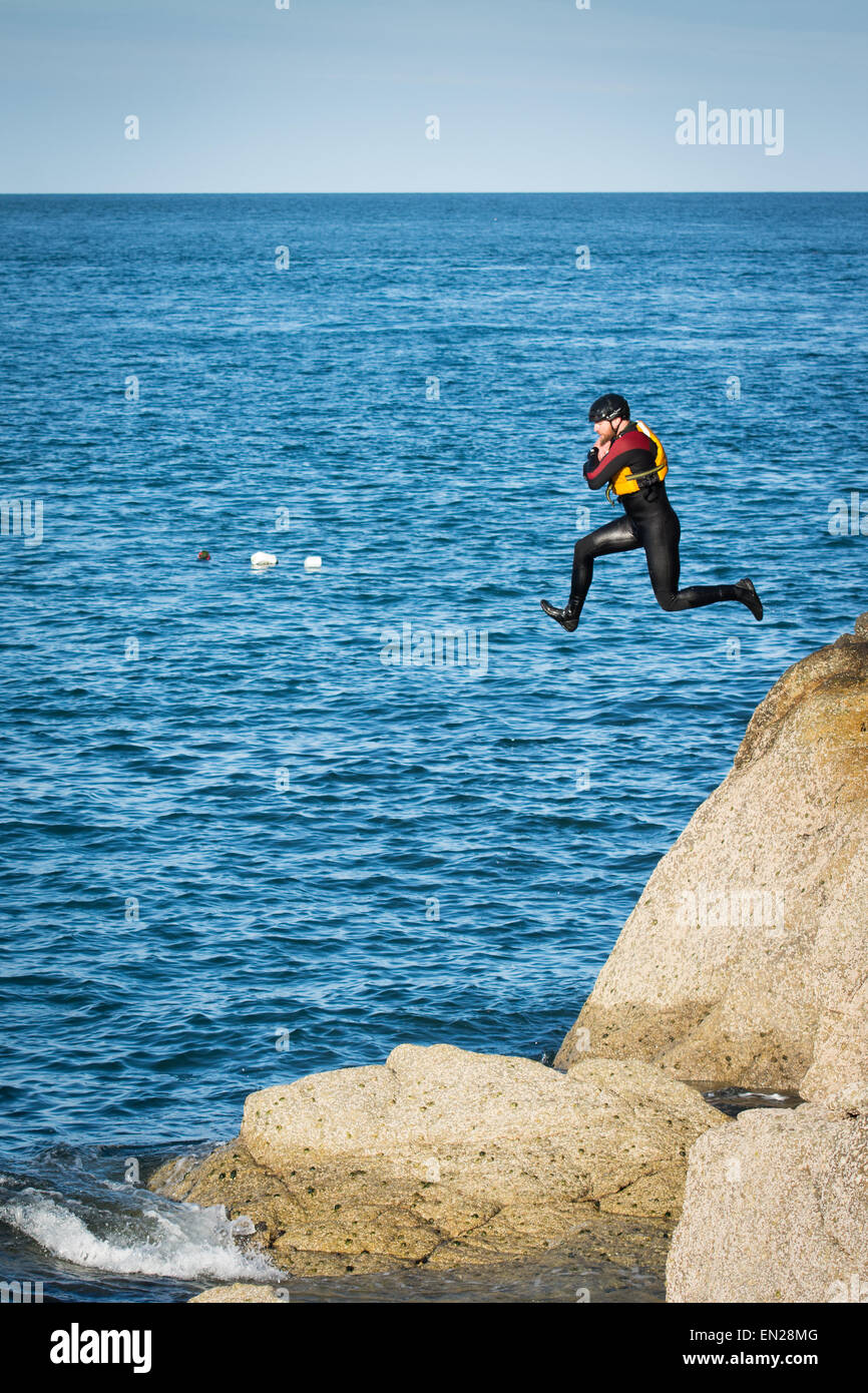 L'homme en combinaison, casque et gilet de sauter des rochers dans la pratique de la mer l'un des sports coasteering. Banque D'Images