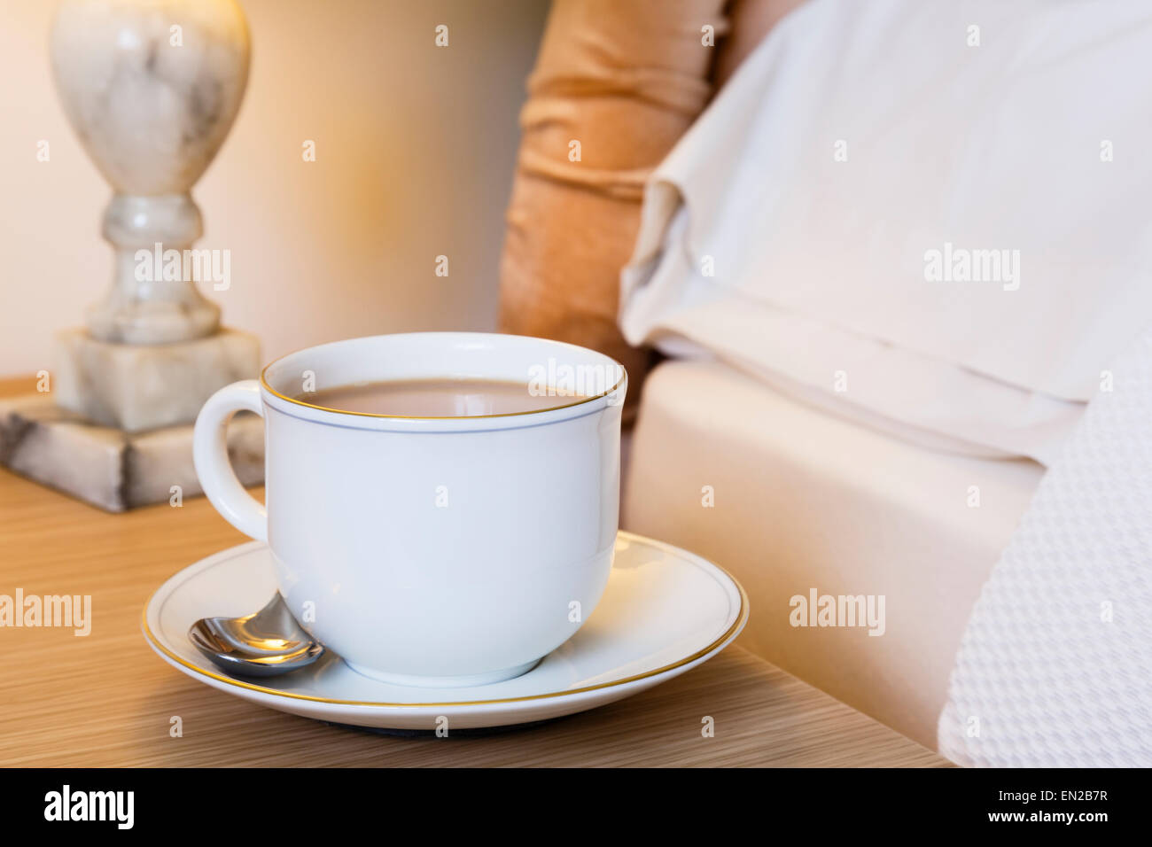 Tasse de thé et soucoupe du matin anglais sur une table de chevet sur le côté d'un lit. Style de vie quotidien. Angleterre Royaume-Uni Grande-Bretagne Banque D'Images