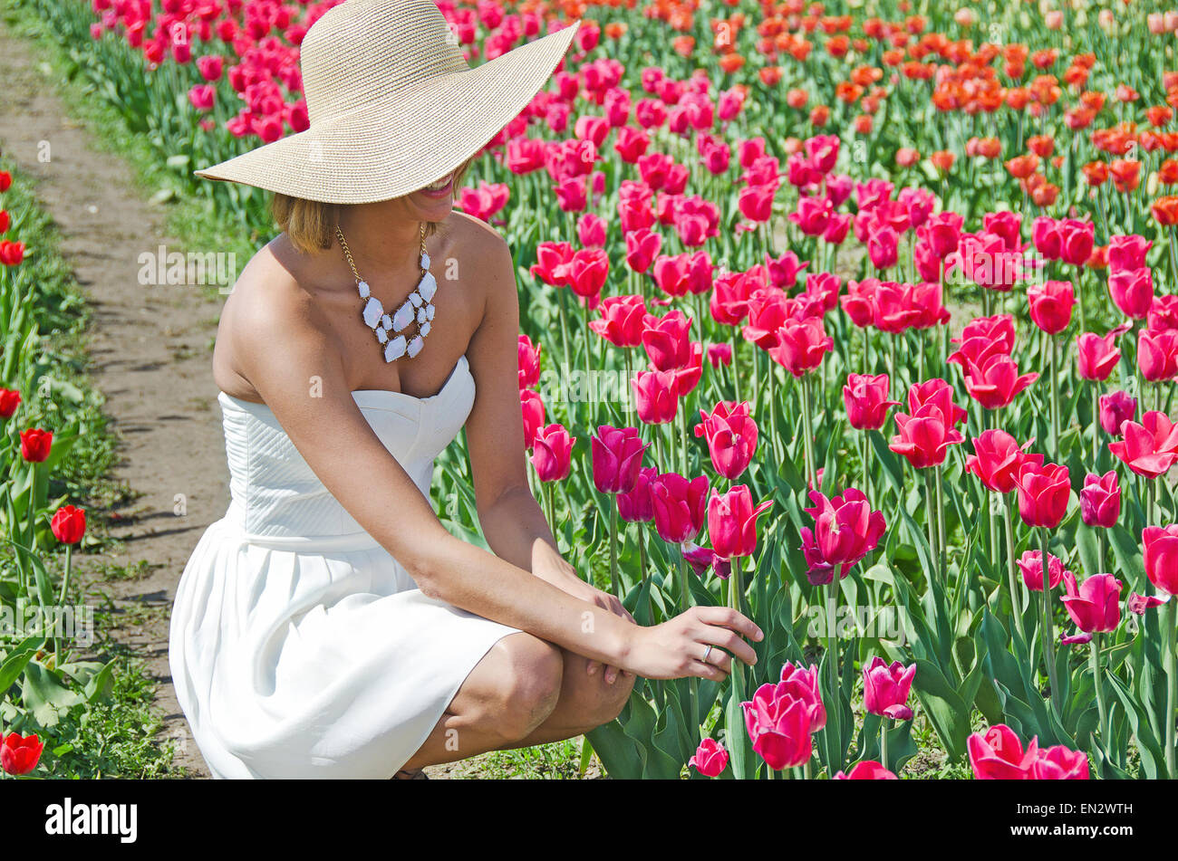 Jolie femme avec fashion hat et white bretelles robe d'été dans un jardin de tulipes au printemps. Banque D'Images
