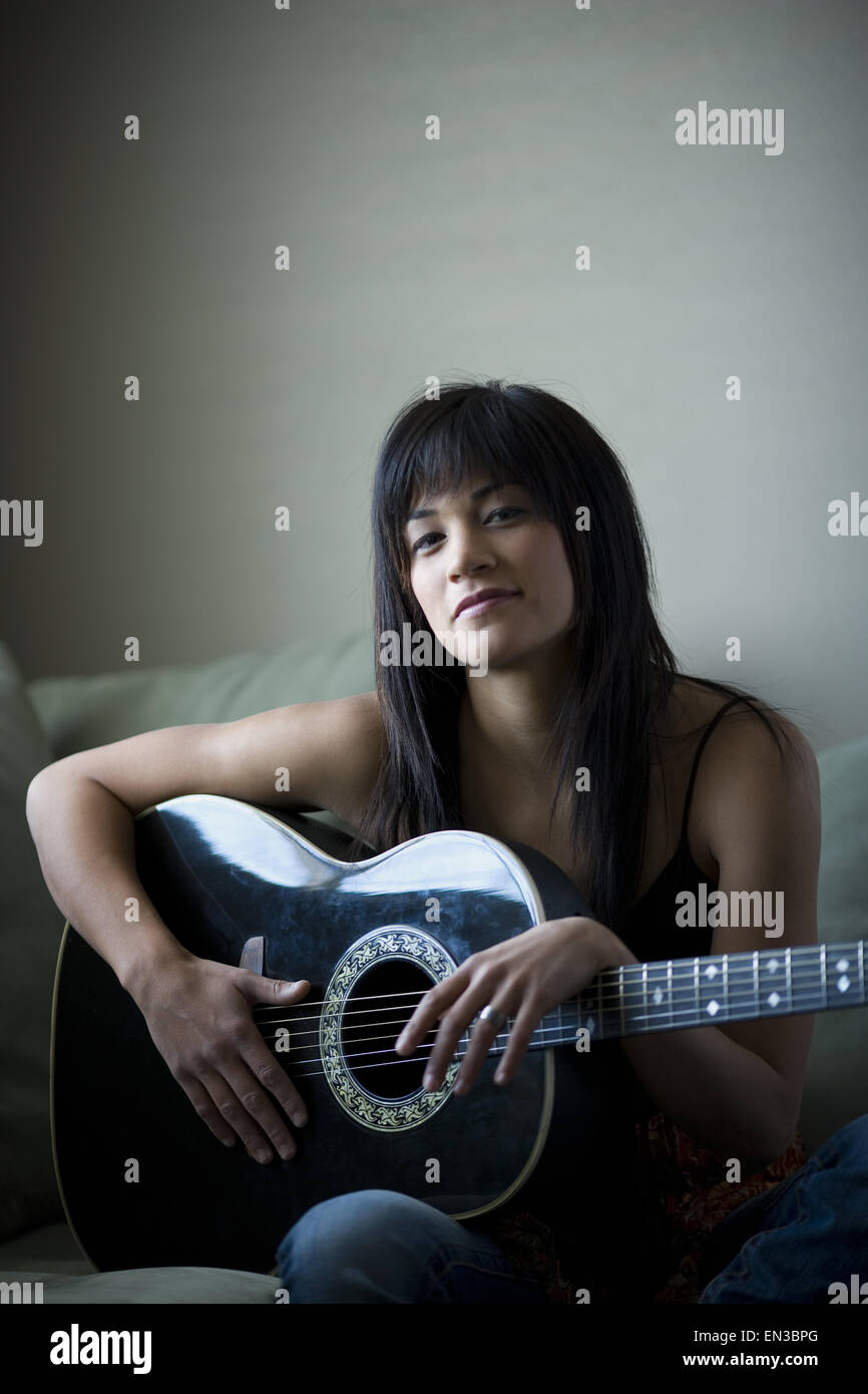 Woman sitting on sofa holding guitar smiling Banque D'Images