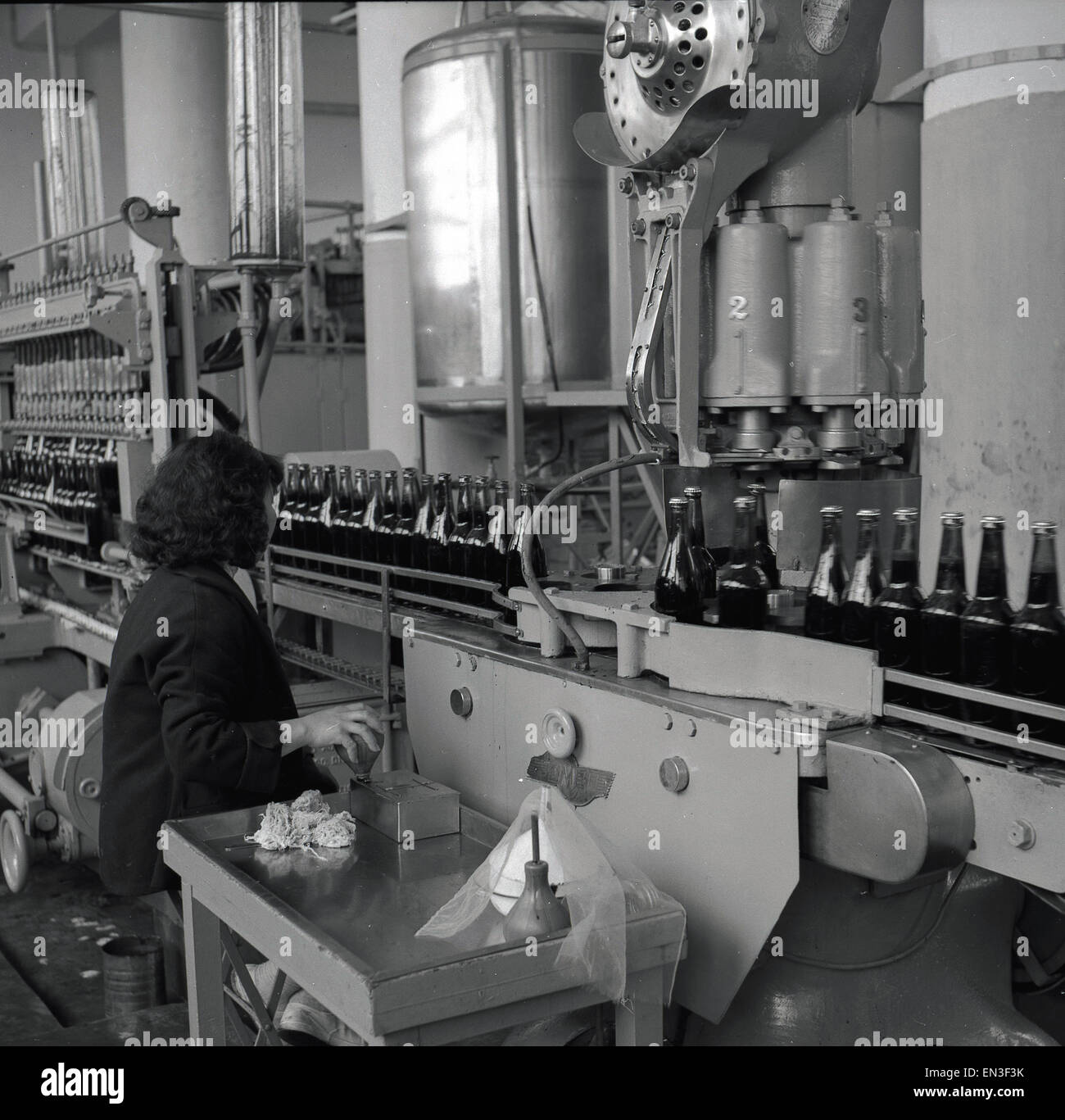 Historique années 1950, dame l'utilisation d'une machine à une usine d'embouteillage. La machine est de mettre les couvercles sur les bouteilles de verre Banque D'Images