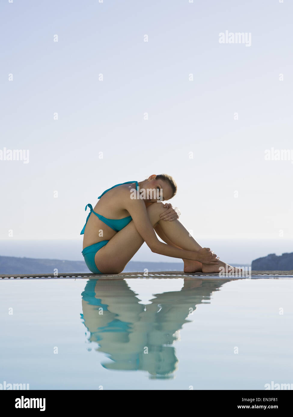 Woman in swimsuit assis à bord de piscine à débordement en plein air Banque D'Images
