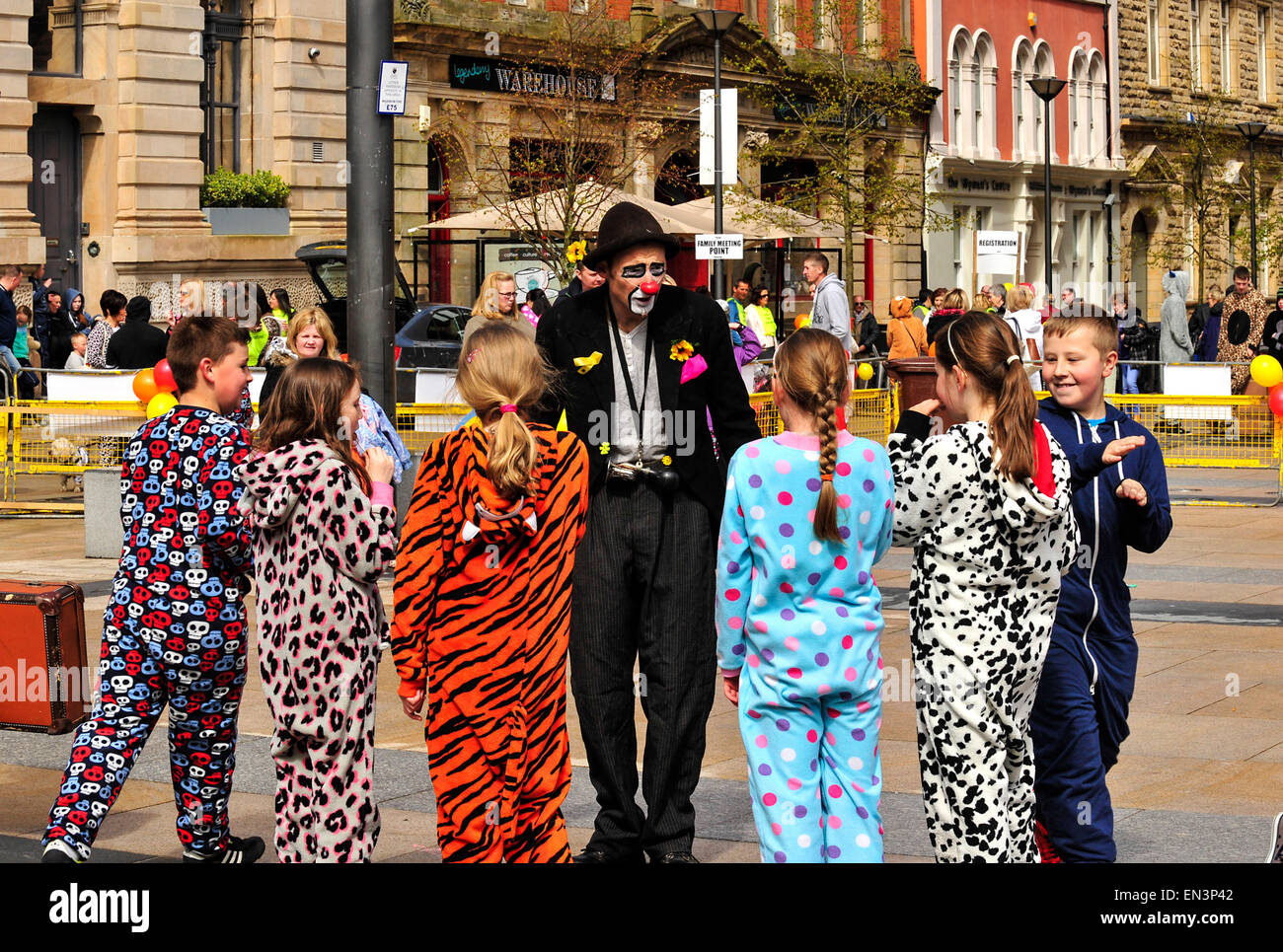 Clown avec visage peint, nez rouge et portant un chapeau Amusant les enfants habillés en onesies dans le Guildhall Square, Derry, Lon Banque D'Images