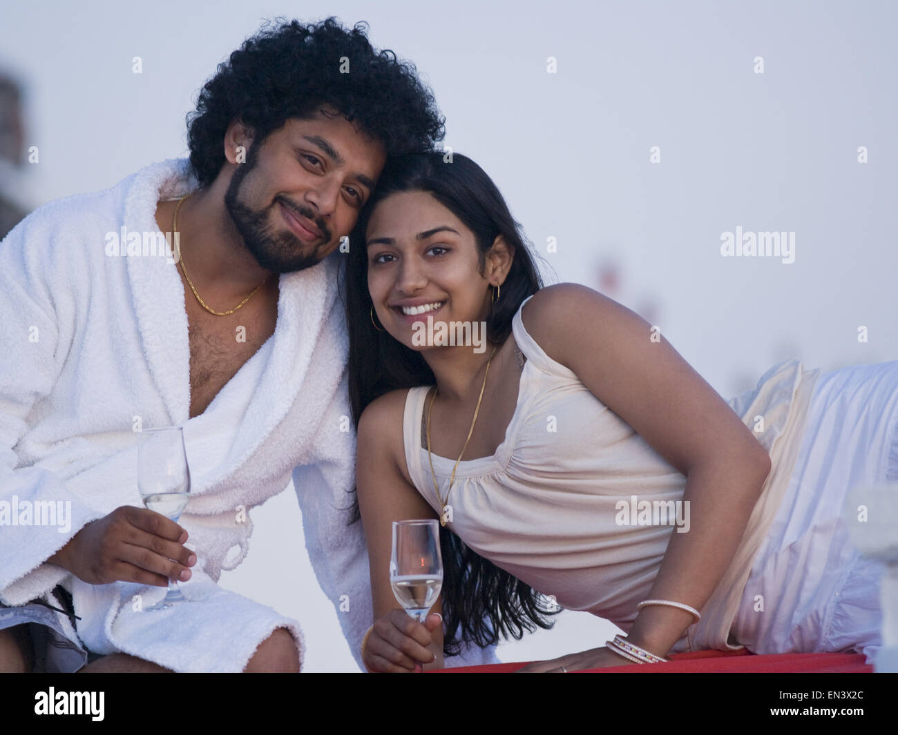 Couple assis en plein air avec des flûtes à champagne en souriant et se pelotonnant Banque D'Images