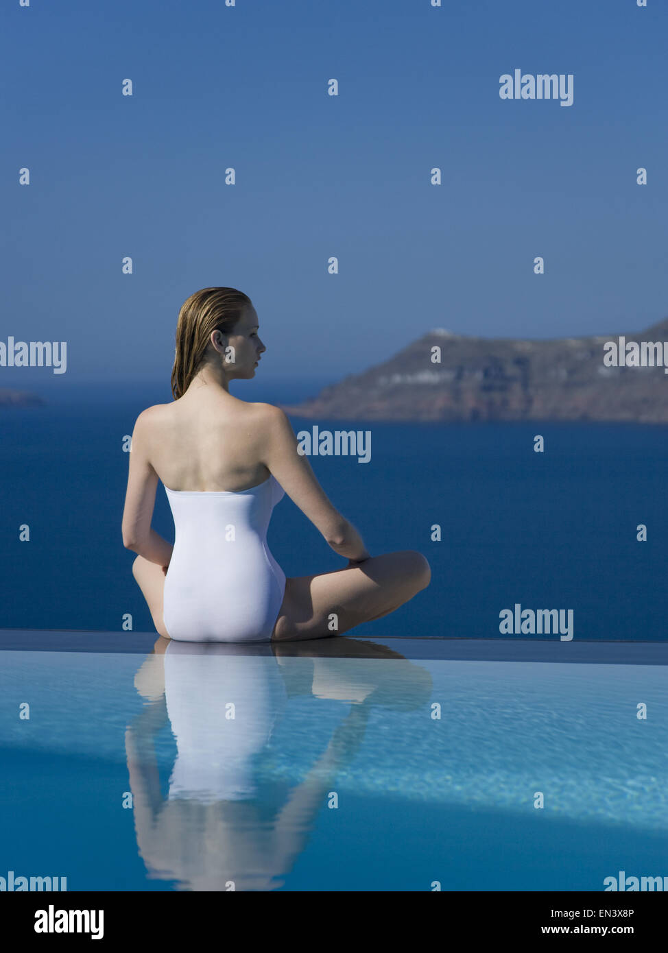 Woman in swimsuit sitting cross legged par piscine à débordement en plein air Banque D'Images