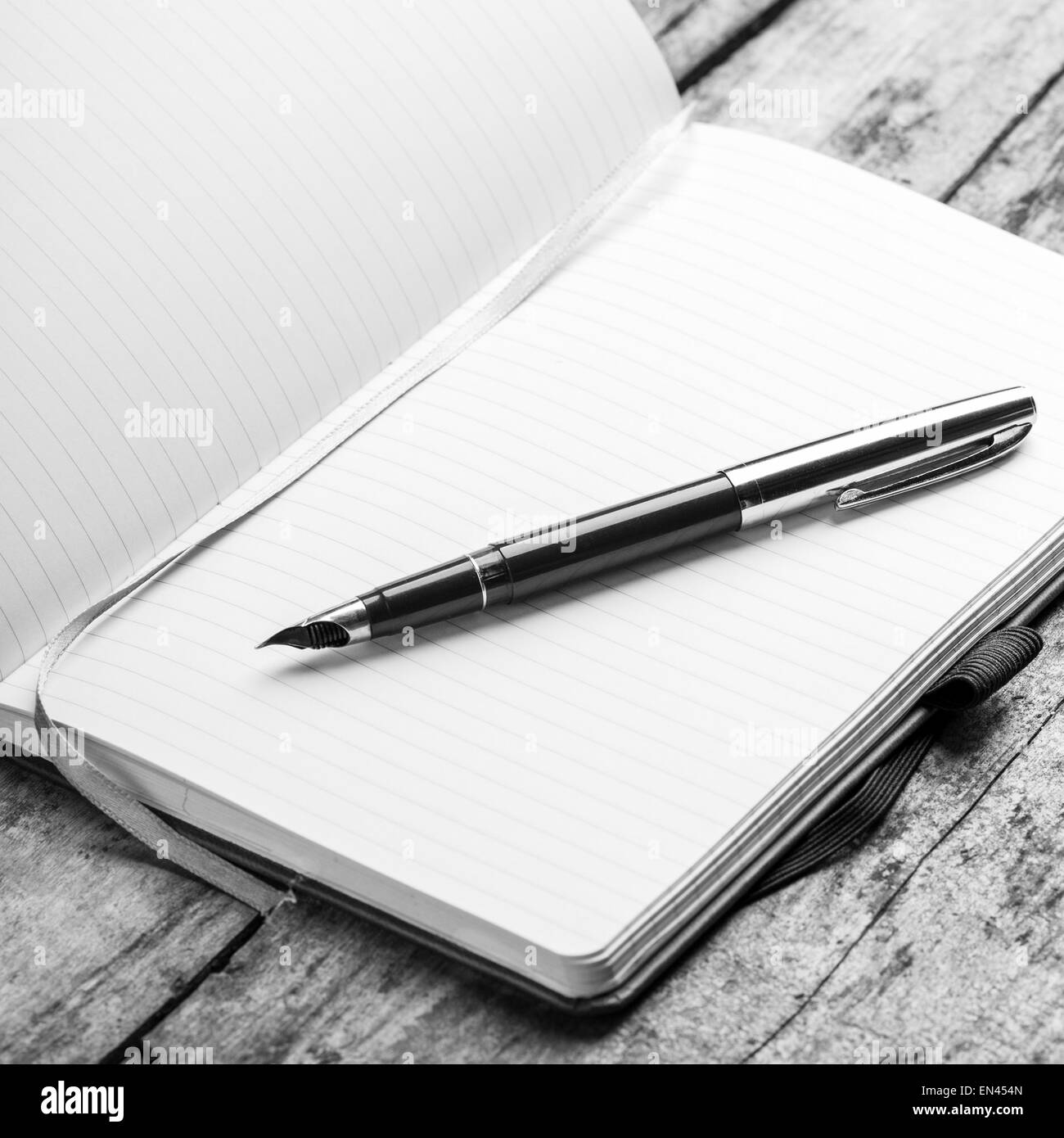 Ordinateur portable blanc ouvert avec un élégant stylo doré sur fond de bois. Image en noir et blanc Banque D'Images