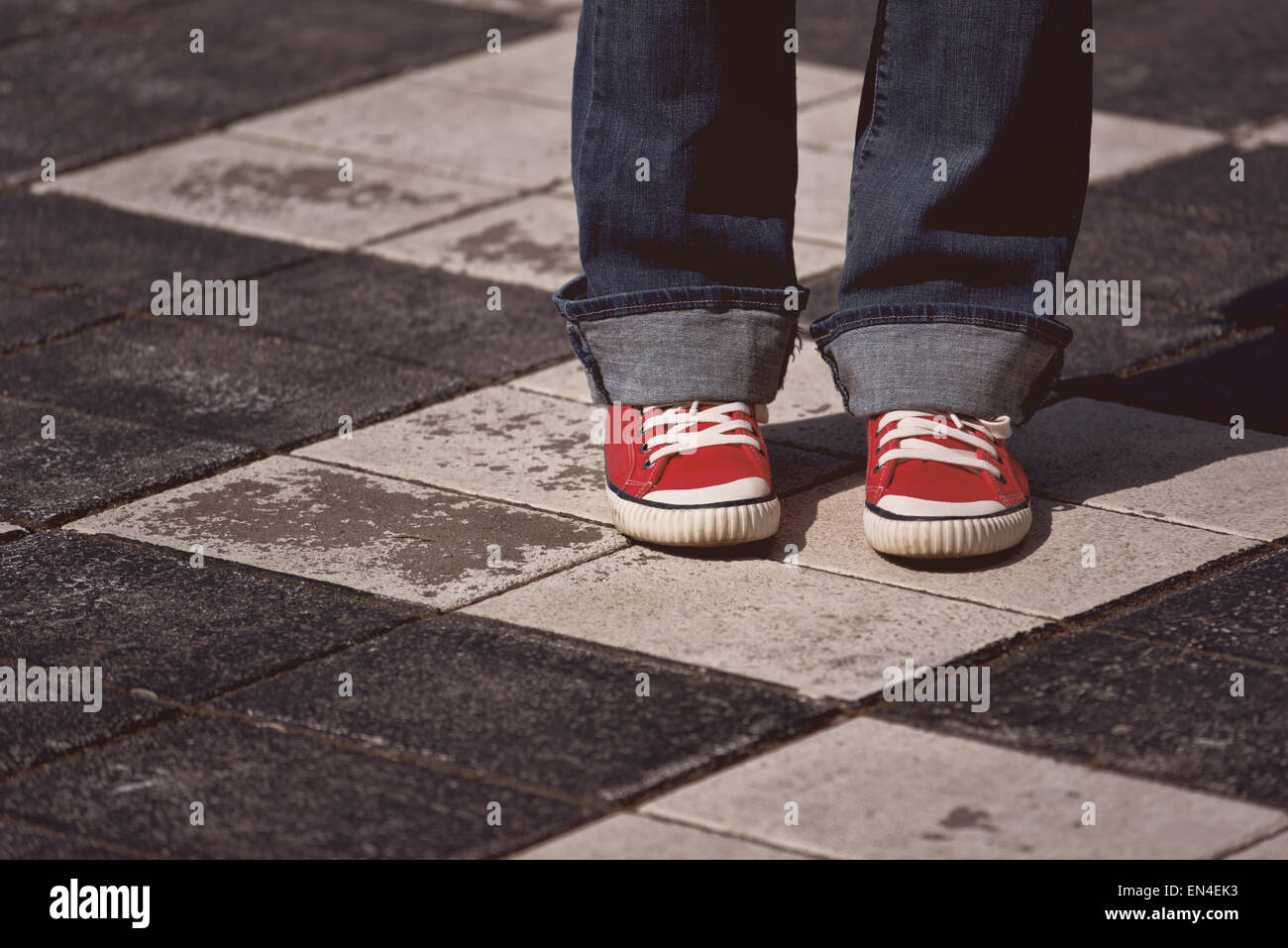 Les jambes de jeunes adolescentes en rouge sneakers debout sur la rue sur la chaussée à carreaux comme des échecs, tonique libre avec Banque D'Images