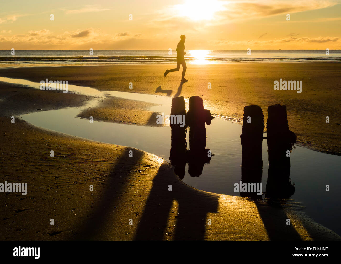 Homme qui court sur la plage au lever du soleil à Sandsend, North Yorkshire, UK. Banque D'Images