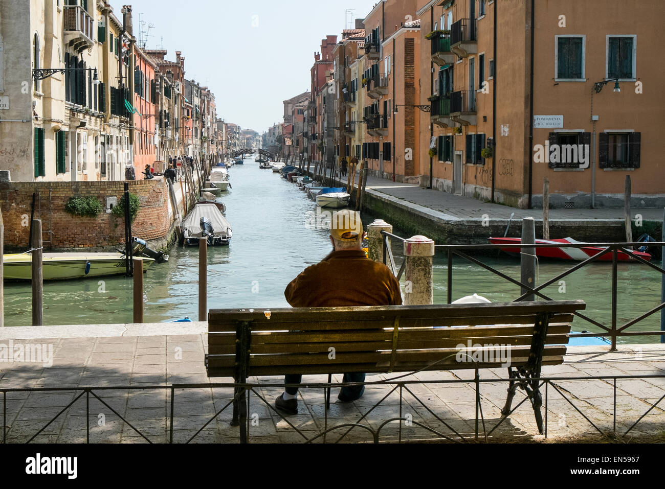 Un homme assis sur le banc en face d'un canal à Venise Banque D'Images