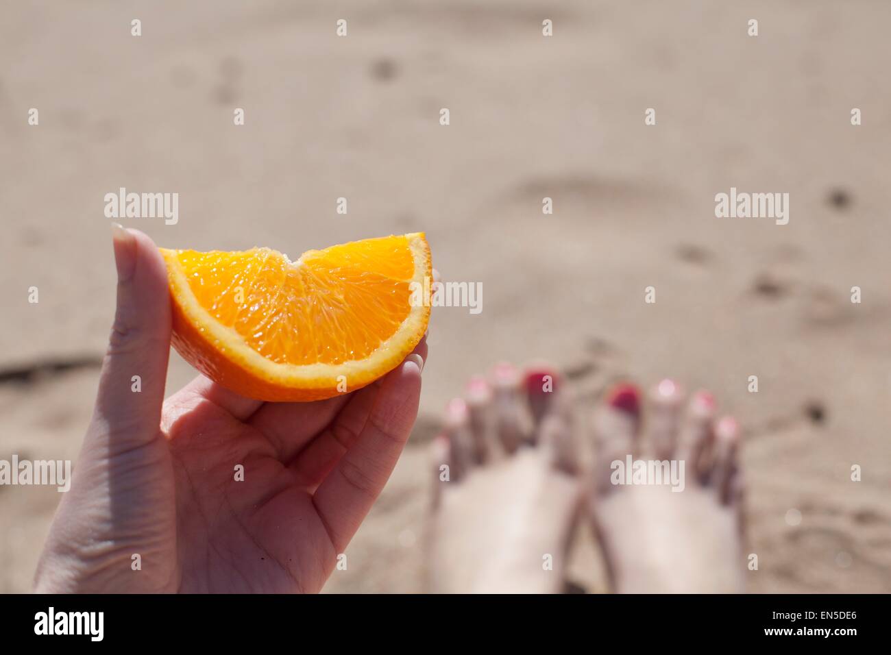 Main tenant une orange segment sur une plage, vue de jambes Banque D'Images