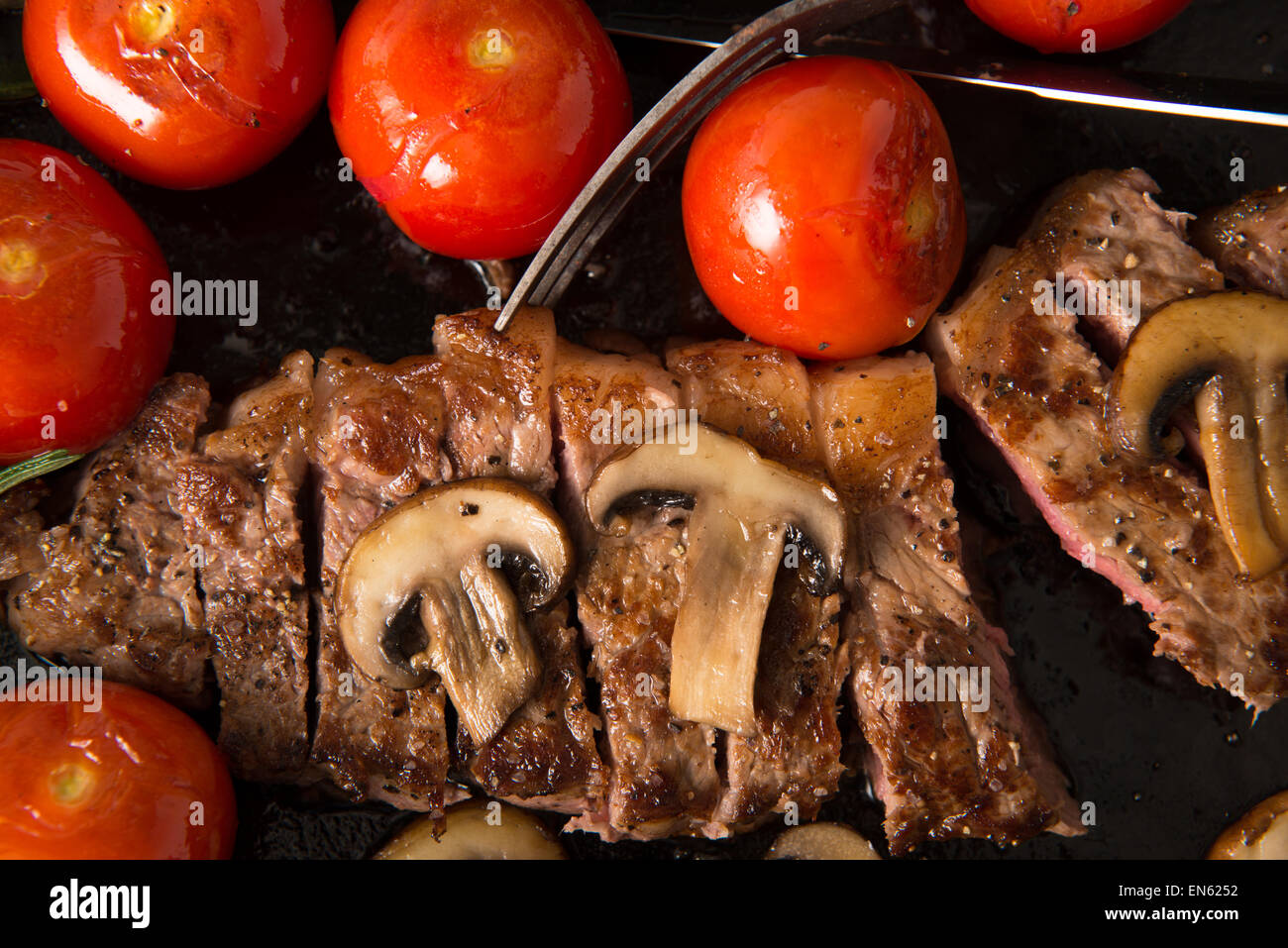 Contre-filet de cuisson dans la poêle en fonte : Steak est cuites et tranchées - illustré avec des tomates grillées et champignons Banque D'Images