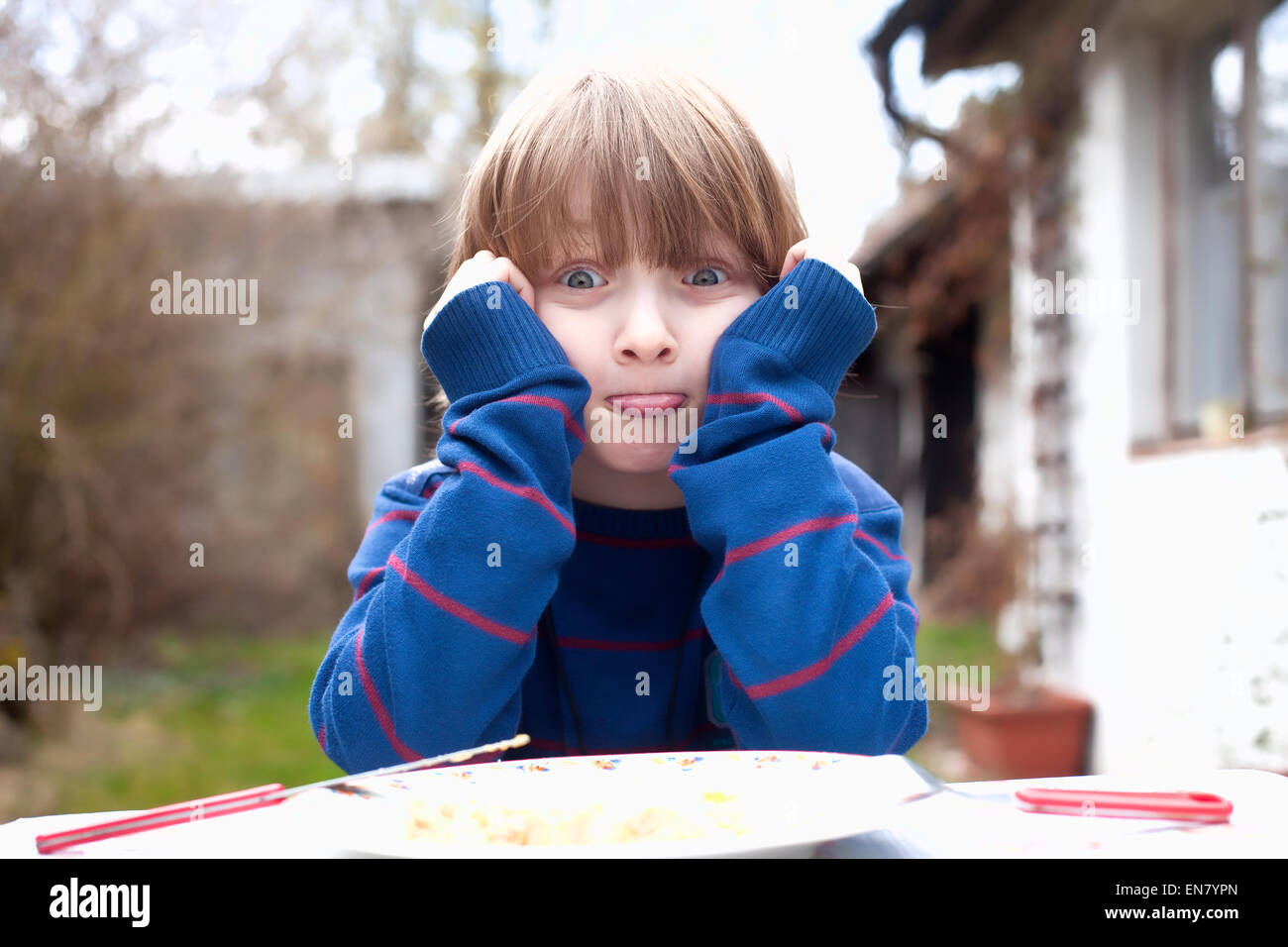 Boy Eating Outdoors Making Faces Banque D'Images