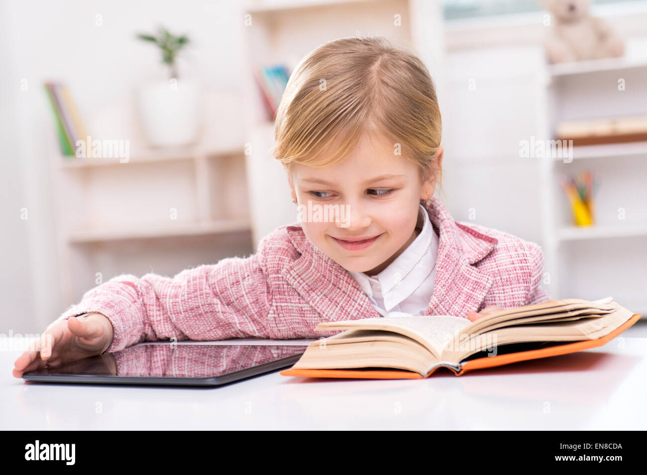 Petite fille essayant de choisir entre livre et ordinateur tablette Banque D'Images
