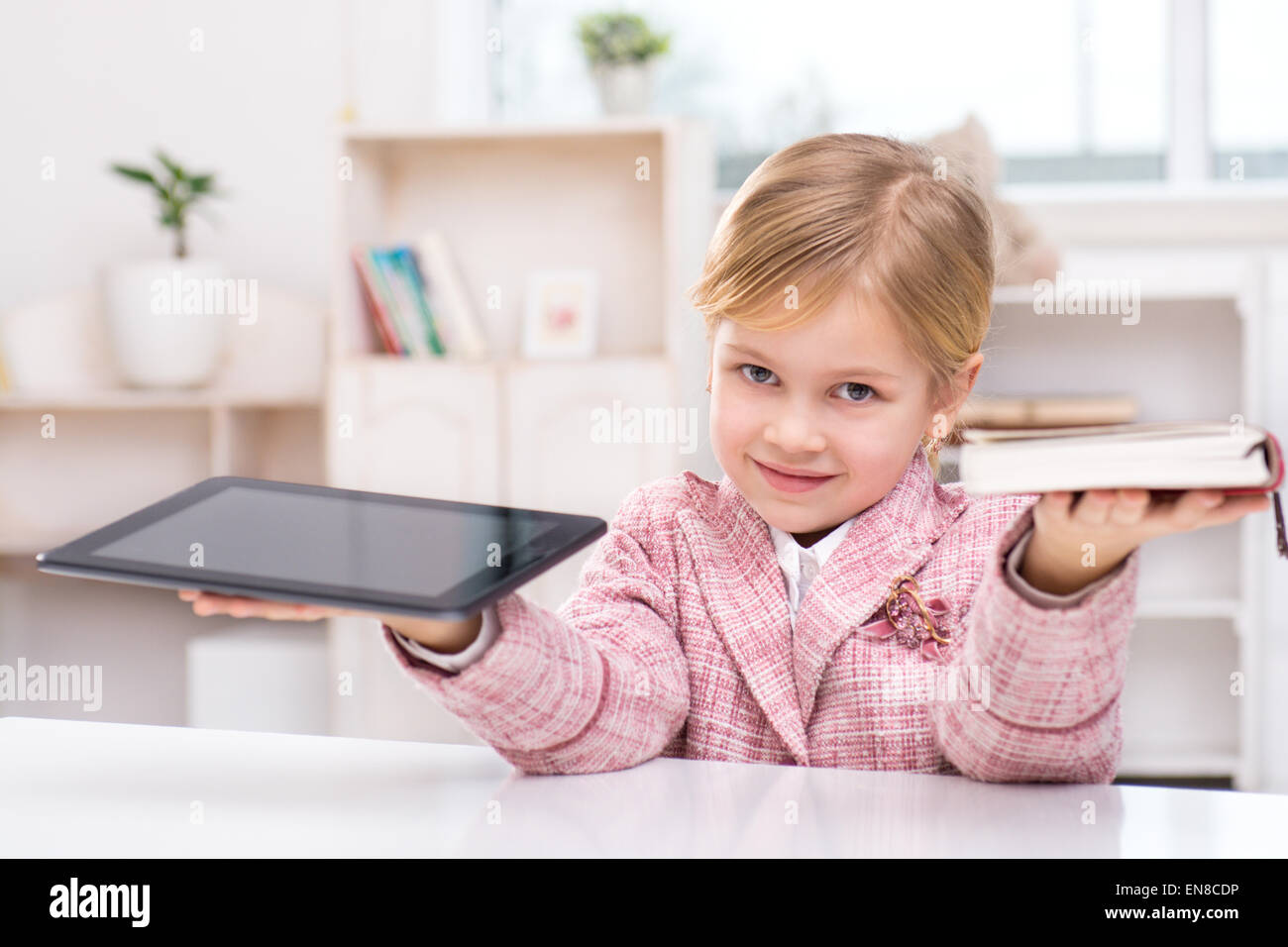 Petite fille essayant de choisir entre livre et ordinateur tablette Banque D'Images