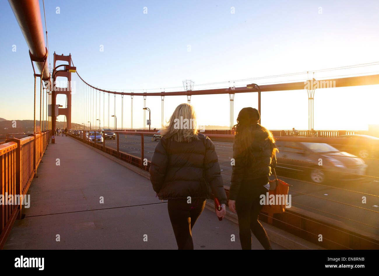Deux femmes marcher sur le Golden Gate Bridge à la circulation à l'arrière-plan de San Francisco Californie au coucher du soleil. Banque D'Images