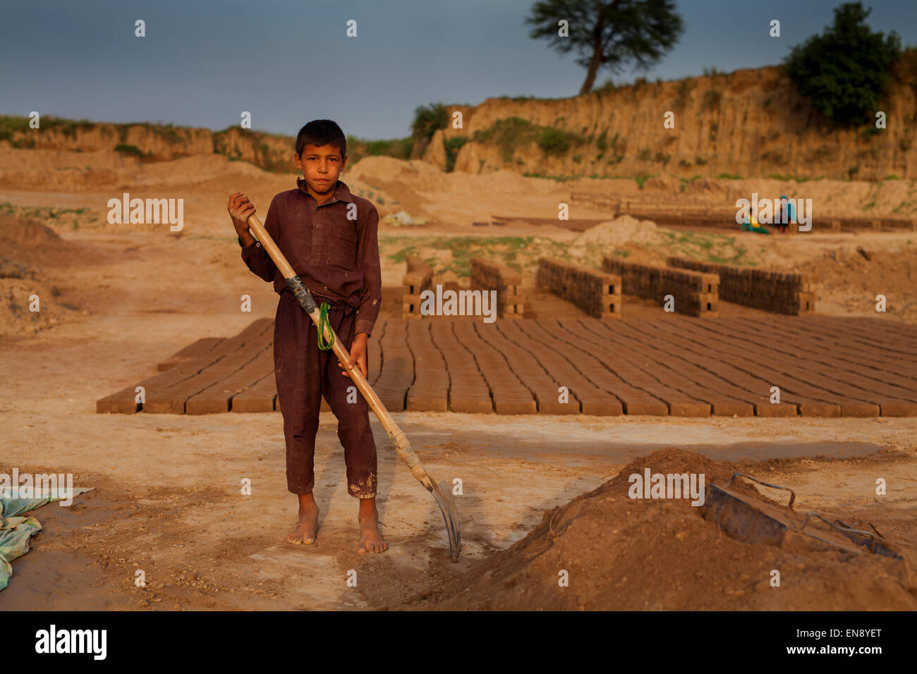 Un enfant travailleur tenant une pelle à l'installation de fabrication de briques Banque D'Images