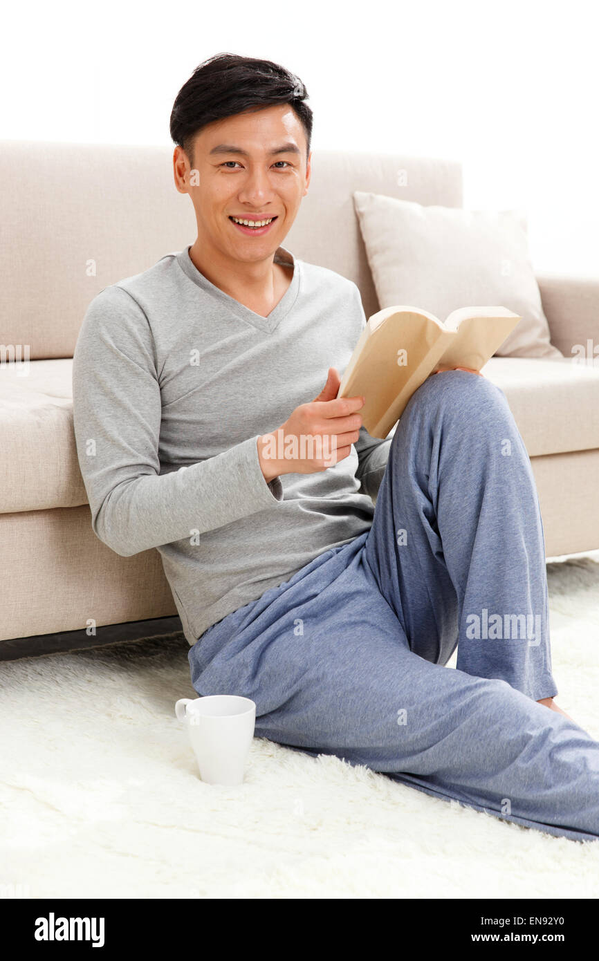 Jeune homme assis sur le sol et lire un livre Banque D'Images