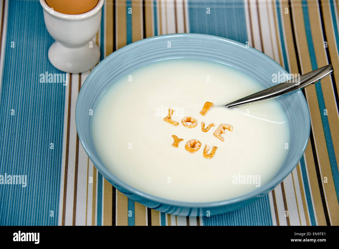 Message d'amour en céréales petit déjeuner bol flottant dans le lait blanc avec cuillère et brown oeuf dur. Banque D'Images Message d'amour en céréales petit déjeuner bol flottant dans le lait blanc avec cuillère et brown oeuf dur. Banque D'Images