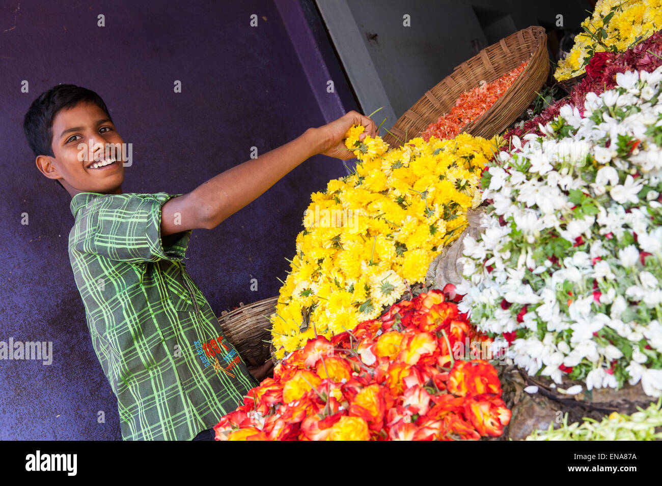 A smiling boy prépare un écran de fleurs et de guirlandes at a market stall à Nandyal Banque D'Images