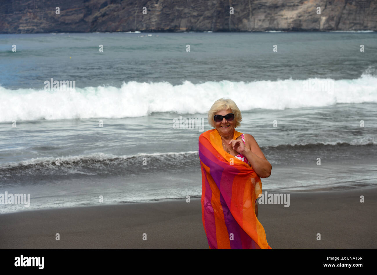 Portrait d'une femme âgée qui est debout sur le sable noir de Guios volcanogène plage avec wrap o n l'épaule sur surf wa Banque D'Images