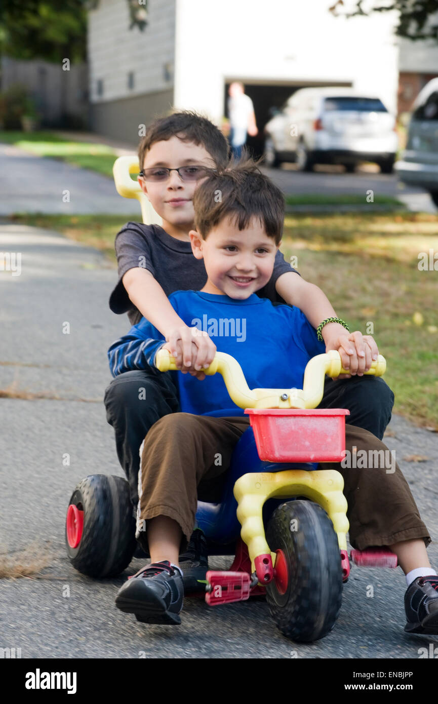 Deux frères, l'âge de sept et quatre ride une grande roue à trois roues dans leur garage. Banque D'Images
