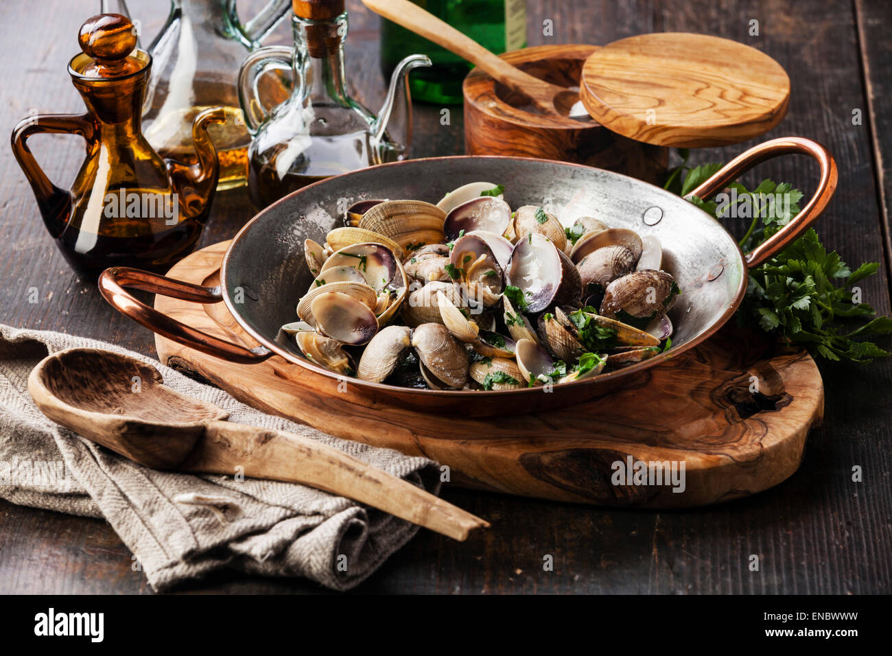 Vongole coquilles de palourdes Vénus avec le persil dans le plat de cuisson en cuivre foncé sur fond de bois Banque D'Images