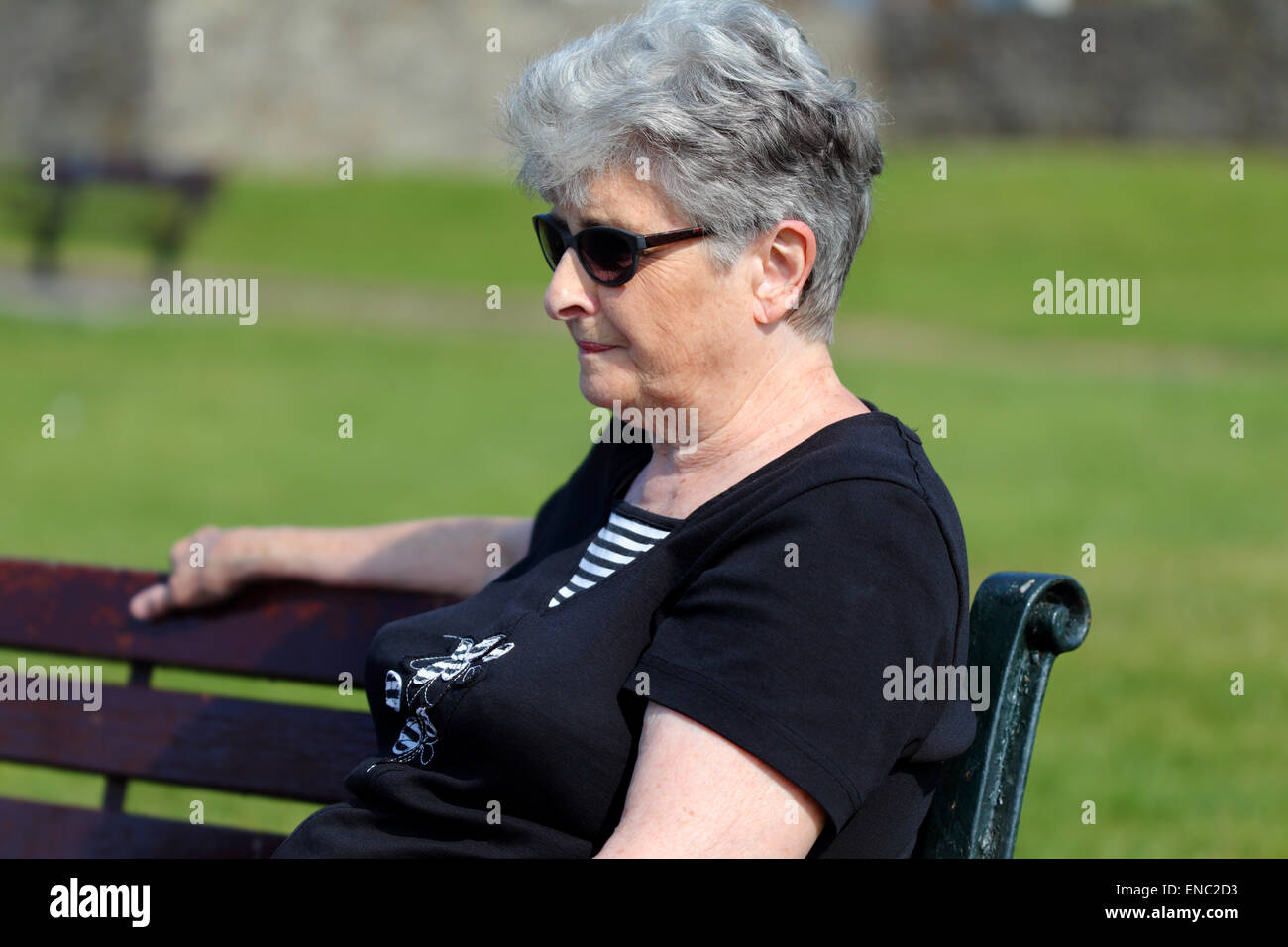 Dame plus âgée se détend à l'extérieur sur un banc de parc Banque D'Images