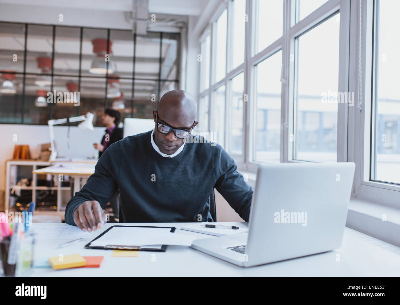 Jeunes cadres assis à son bureau avec ordinateur portable la lecture d'un document. African man working in office. Banque D'Images