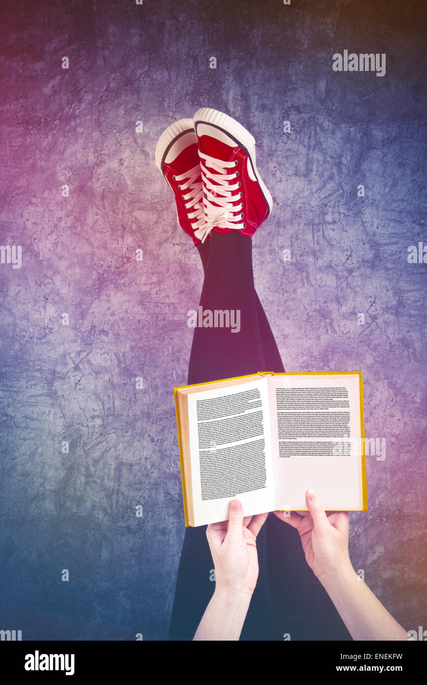 Jeune femme lisant Pulp Fiction livre avec ses pieds soulevés en l'air, sur les pages de texte générique Banque D'Images