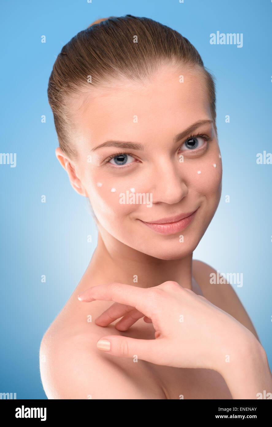 Woman lifting crème sur le visage, sur fond bleu. Photographie haute résolution Banque D'Images