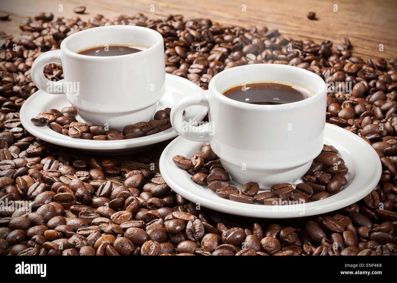 Deux tasses de café parmi les grains de café sur une table en bois. Banque D'Images
